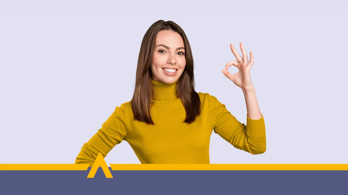 kobieta prezentująca gest OK z uśmiechem, ubrana w musztardowy golf